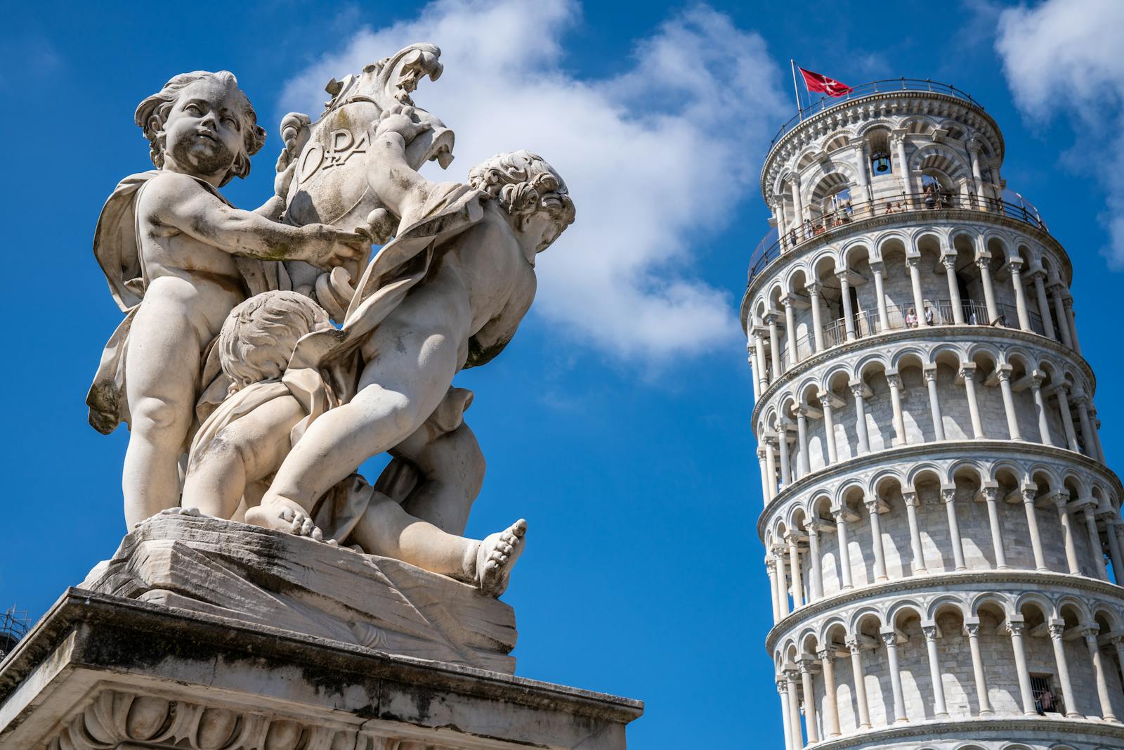 Vista dal basso della Torre di Pisa e di una statua